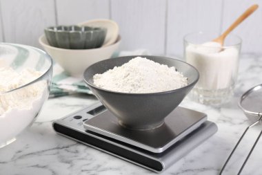 Dijital mutfak terazisi, beyaz mermer masa üzerinde bir kase un ve diğer ürünler, yakın plan.