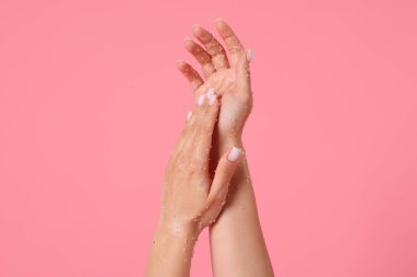 Pembe arka planda ellerini ovuşturan kadın, yakın plan.