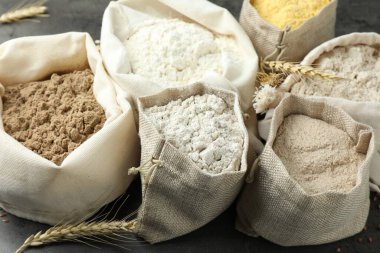 Gri masadaki çantalarda farklı tipte un, yakın plan.