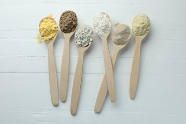 Beyaz ahşap masadaki kaşıklarda farklı türde un, düz.