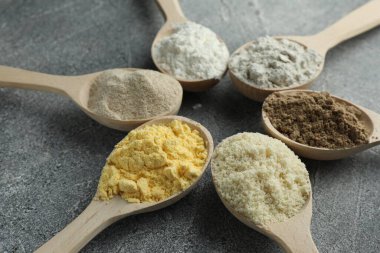Gri masadaki kaşıklarda farklı türde un, yakın plan.