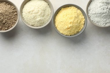 Açık gri masadaki kaselerdeki farklı un türleri, düz yatış. Metin için boşluk