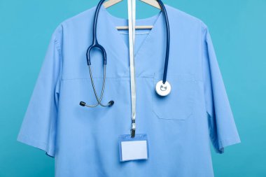 Steteskop ve rozetli sağlık çalışanı üniforması mavi arka planda.