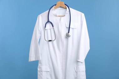 Mavi arka planda asılı steteskoplu doktor ceketi.