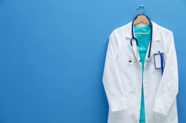 Steteskop ve rozetli doktorun ceketi mavi arka planda. Metin için boşluk