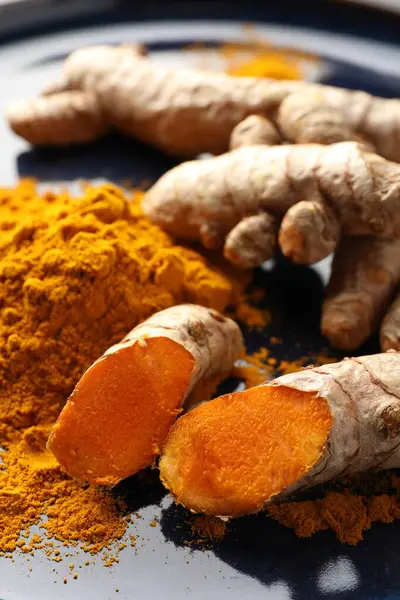 Aromatik zerdeçal tozu ve mavi tabakta taze kökler, yakın plan.
