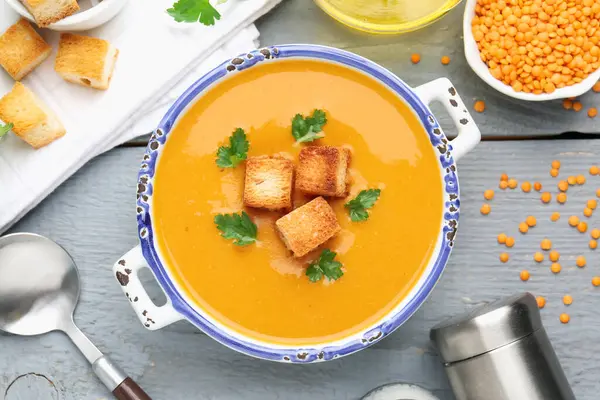 Lezzetli mercimek kremalı çorba. Gri ahşap masada kızarmış ekmeklerle servis ediliyor.