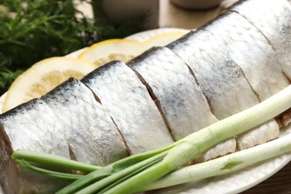 Limon dilimli lezzetli ringa balıkları, yeşil soğan ve ahşap masada dereotu, yakın plan.
