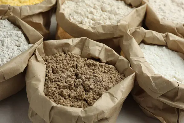 Beyaz masadaki kağıt torbalarda farklı türde un, yakın plan.
