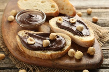 Çikolata sürülmüş ekmek dilimleri ve ahşap masada fındıklar, yakın plan.