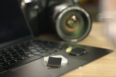 SD hafıza kartları, tutucu, dizüstü bilgisayar ve fotoğraf makinesi ahşap masada, yakın plan.