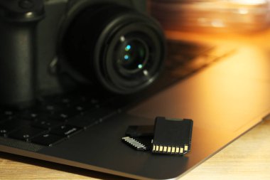 SD hafıza kartları, dizüstü bilgisayar ve fotoğraf makinesi ahşap masada, yakın plan.