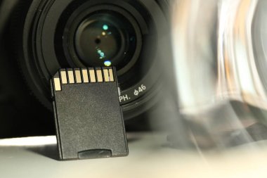 SD hafıza kartı ve fotoğraf makinesi beyaz masada, yakın plan.