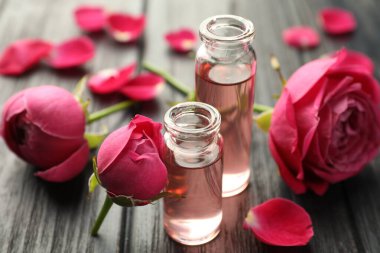 Aromatik esanslı parfüm şişelerini aç ve gri ahşap masada güller, yakın plan.