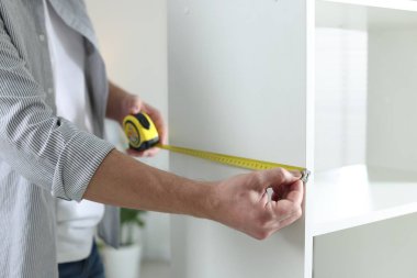 Beyaz rafları bantla ölçen adam içeride, yakın plan.