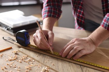 Kapalı alanda bant ile ahşap kalas ölçen bir adam.