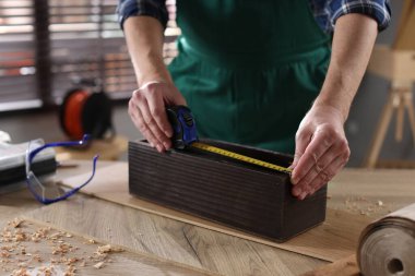 İçerideki ahşap masada bant ile ölçüm yapan adam, yakın plan.