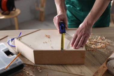 İçerideki masada bantlı ahşap kutuyu ölçen adam, yakın plan.