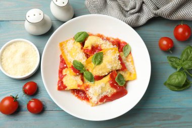 Domates soslu lezzetli ravioli, parmesan peyniri ve fesleğen mavi ahşap masada, düz yerde.