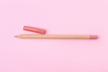 Açık pembe arka planda güzel bir dudak kalemi, üst manzara.