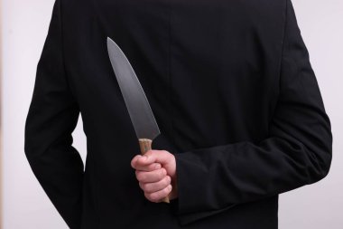 Beyaz arka planda sırtında bıçak tutan iş adamı, yakın plan.
