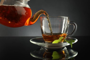 Çaydanlıktan taze demlenmiş çayı siyah masaya, cam fincana dökerek.