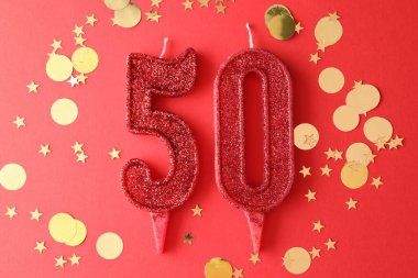 50th birthday. Number shaped candles and confetti on red background, flat lay