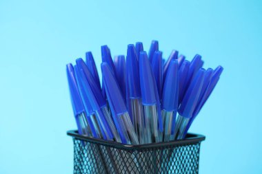 Many ballpoint pens in holder on light blue background, closeup