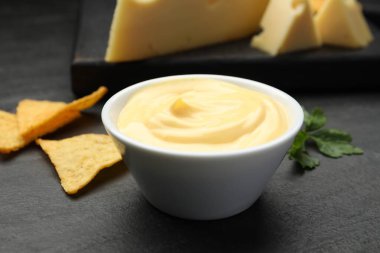 Peynir sosunu kaseye daldırmak, cips ve maydanozu siyah masaya koymak, yakın plan.