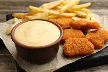 Tabakta nefis peynir sosu, tavuk nugget ve ahşap masada patates kızartması, yakın plan.