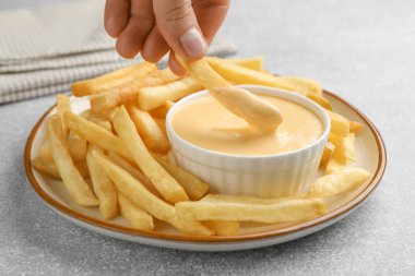 Gri masada patates kızartmasını peynir sosuna batıran kadın, yakın plan.
