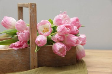 Güzel laleler sepetin içinde ahşap masada, gri arka planda, yakın planda.