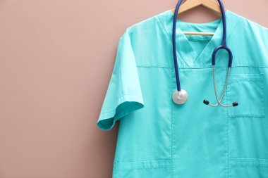 Bej arka planda steteskop takılı sağlık çalışanı üniforması. Metin için boşluk