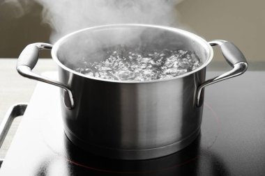 Kaynar suyla pişirme tenceresi ve soba gri arka planda, yakın plan