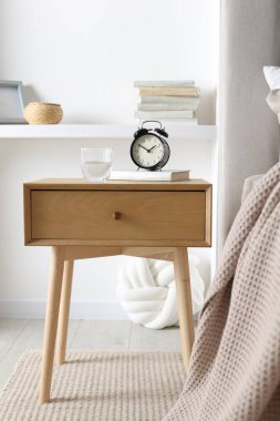 Alarmlı komodinli komodin, bir bardak su ve yatağın yanında kitap.