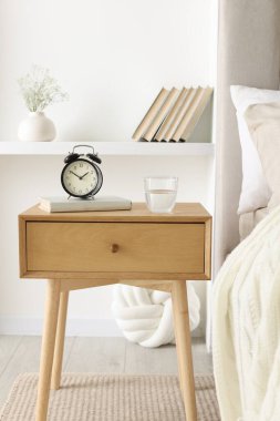 Alarmlı komodinli komodin, bir bardak su ve yatağın yanında kitap.