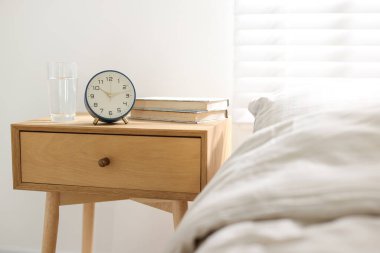 İçinde kitaplar, çalar saat ve yatağın yanında bir bardak su olan komodin.