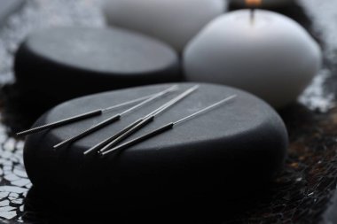 Koyu dokulu arka planda akupunktur iğneleri ve spa taşları, yakın plan