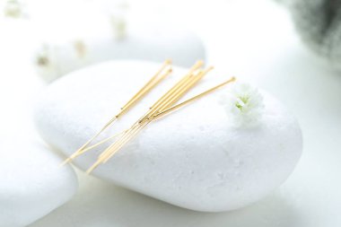 Beyaz arka planda akupunktur iğneleri, çakıl taşı taşı ve çiçek tomurcukları, yakın plan