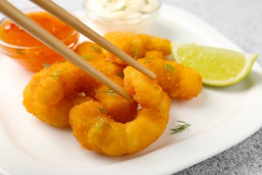 Gri desenli masada tabaktan yemek çubuklarıyla lezzetli tempura karidesleri alıp, yakın plan.