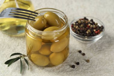 Kavanozda, çatalda, yağda ve biberli yeşil zeytinleri beyaz desenli masada, yakın plan.