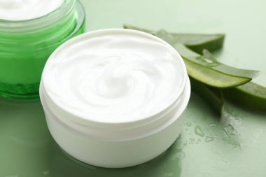 Aloe vera özütüyle nemlendirici krem, yeşil arkaplanda yapraklar ve su damlaları, yakın plan