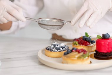 Şekerci, masadaki tartın üzerine pudra şekeri serpiyor, yakın plan.