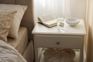 Yatağın yanında kitap, kase ve bir bardak su olan komodinin yanında.