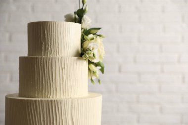 Beyaz tuğla duvarın yanında çiçeklerle süslenmiş nefis düğün pastası, yakın plan. Metin için boşluk