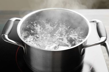Kaynar suyla pişirme tenceresi ve soba gri arka planda, yakın plan