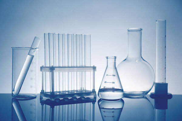 Laboratory glassware with liquid on mirror surface against light background