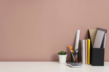 Beyaz ofis masasındaki farklı kırtasiye, çiçek dekoru ve hesap makinesi koyu bej arkaplan, metin için boşluk