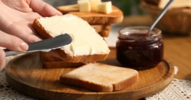 Bir kadın tostun üzerine tereyağı sürüyor.