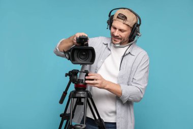 Profesyonel video kamerası ve açık mavi arka planda kulaklığı olan bir adam.